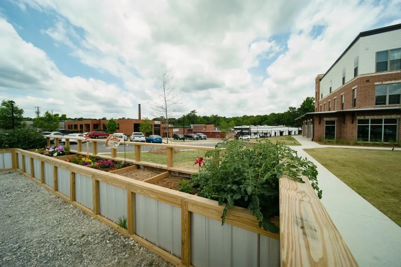 Exterior view of an apartment community with a brick building, sidewalk, and raised garden bed.