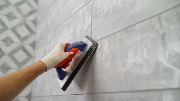 A person is using a sponge to grout a tile wall.