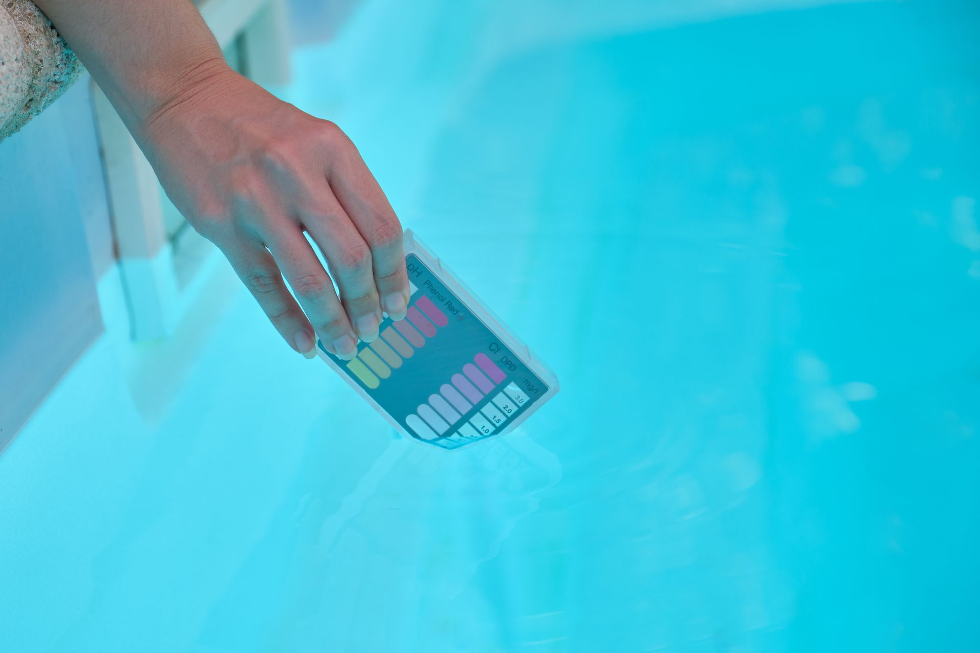 Hand holding a color swatch over bright blue pool water