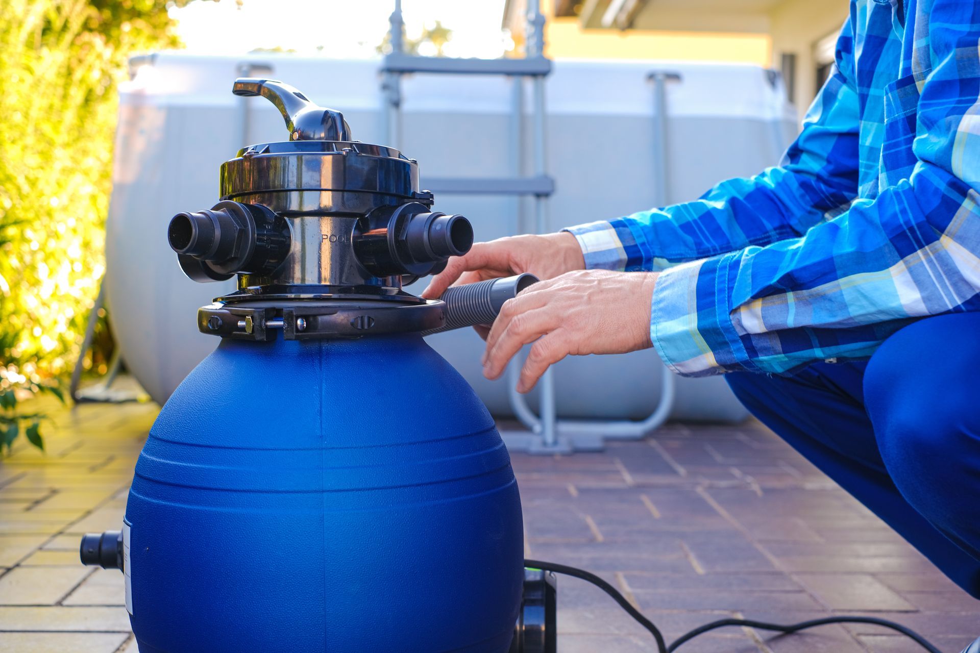 Person adjusting a pool filter valve on a blue tank outdoors