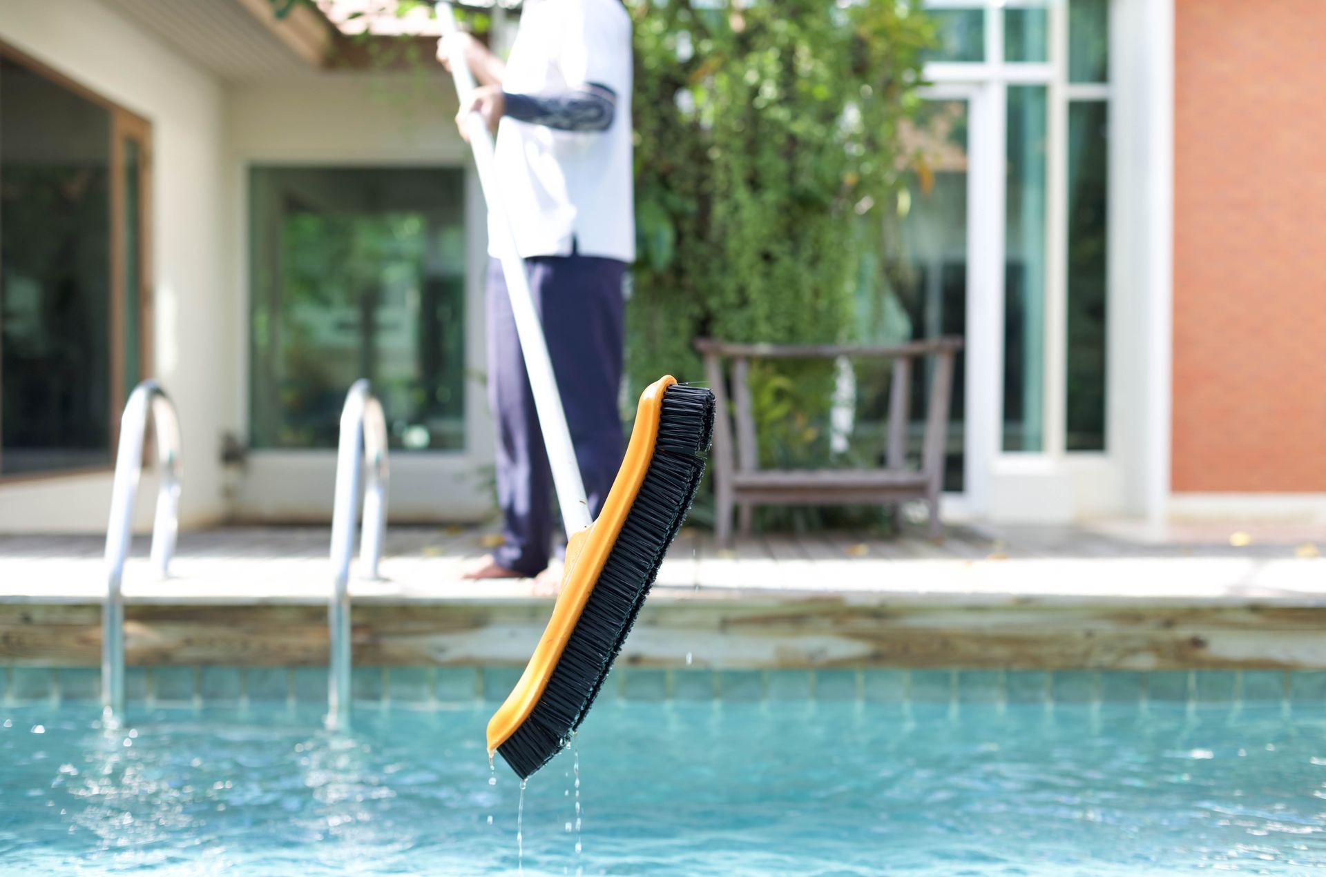 Pool cleaning brush being lifted from a swimming pool, with a person in the background.