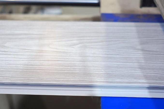 Primer plano de una superficie de metal cepillado con bordes azules sobre un banco de trabajo.
