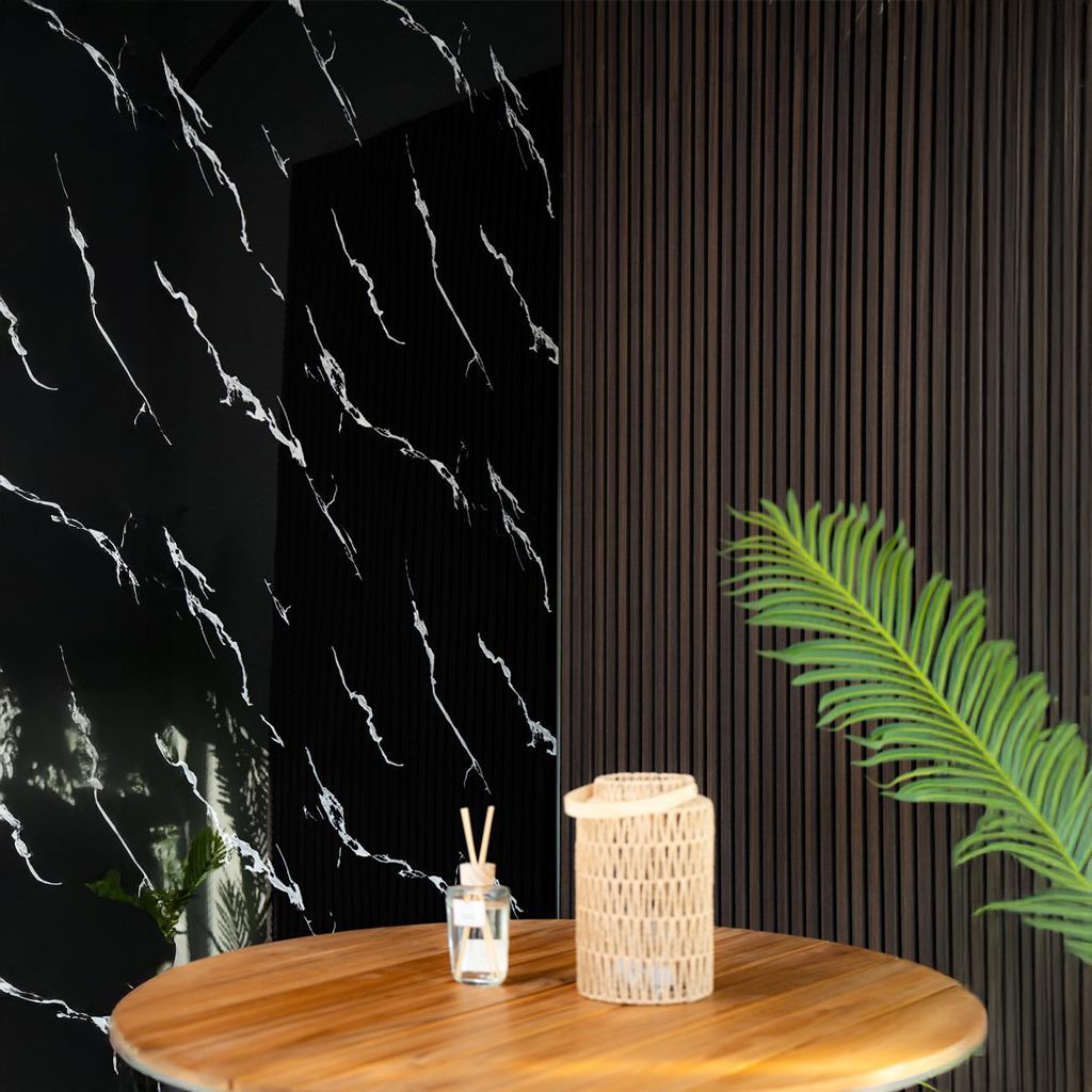 Mesita redonda de madera con elementos decorativos en una habitación moderna: vela, difusor, pared de mármol