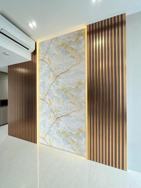 Pared interior moderna con panel de mármol, vetas doradas y listones de madera verticales junto a un aire acondicionado.