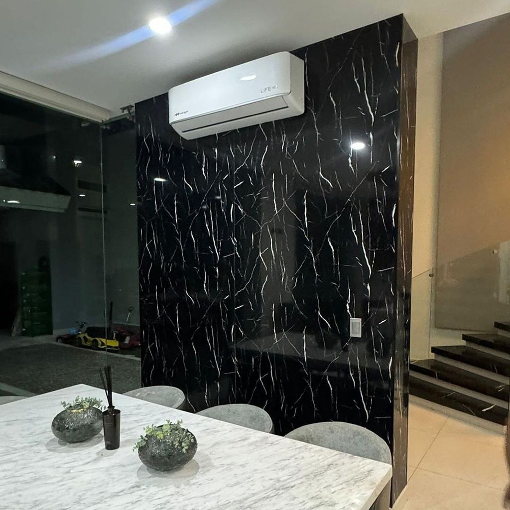 Comedor moderno con pared decorativa de mármol negro, mesa blanca y aire acondicionado mural.
