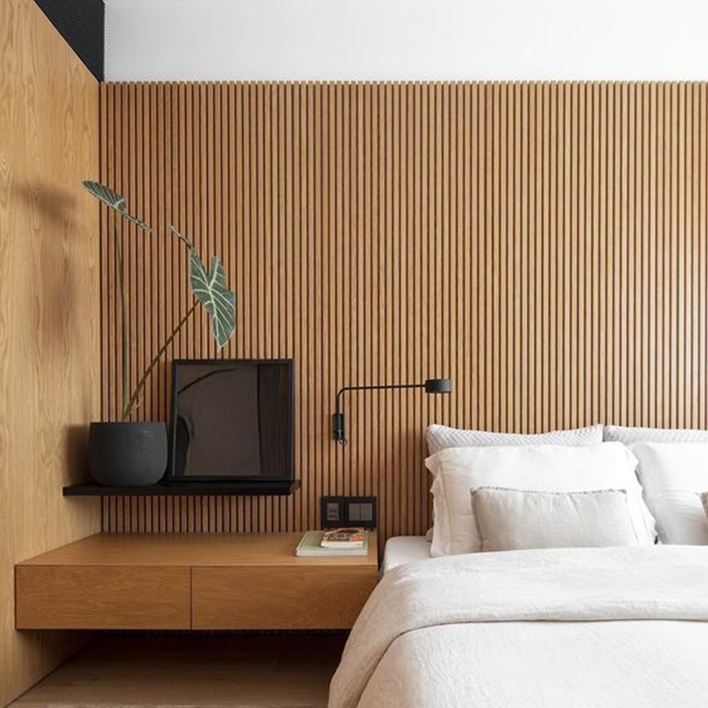 Dormitorio minimalista con sábanas blancas, cabecero de madera en la pared y mesita de noche negra con lámpara de plantas.