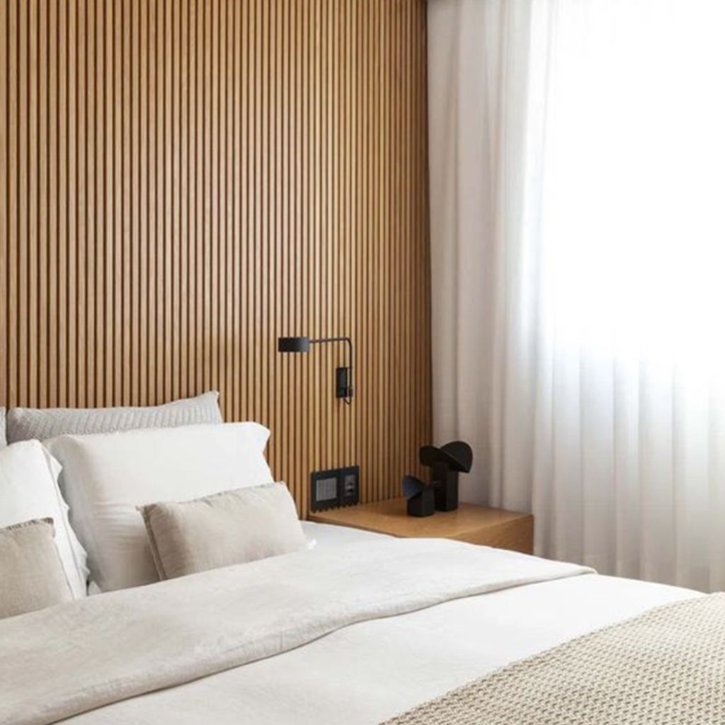 Dormitorio minimalista con sábanas blancas, cabecero de madera en la pared y mesita de noche negra con lámpara de plantas.