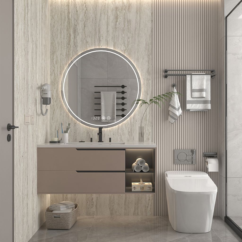 Tocador de baño moderno con espejo redondo iluminado, armario flotante e inodoro sobre paneles de pared a rayas.
