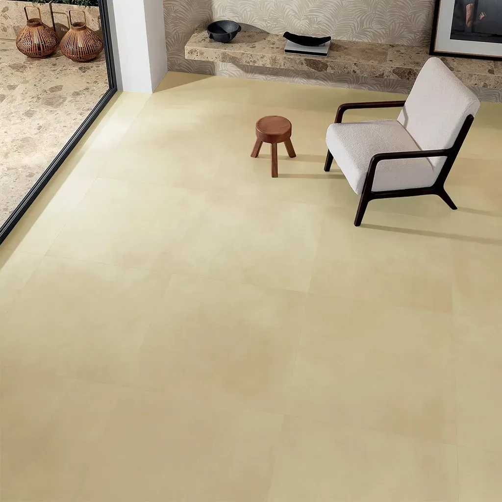 Habitación minimalista con suelo color crema, silla beige, pequeño taburete de madera y una estantería con cojines.