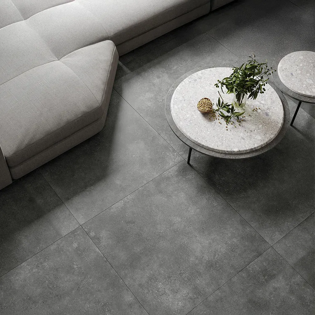 Sala de estar moderna con sofá gris, mesas de centro redondas de mármol y una planta en maceta sobre un suelo gris.
