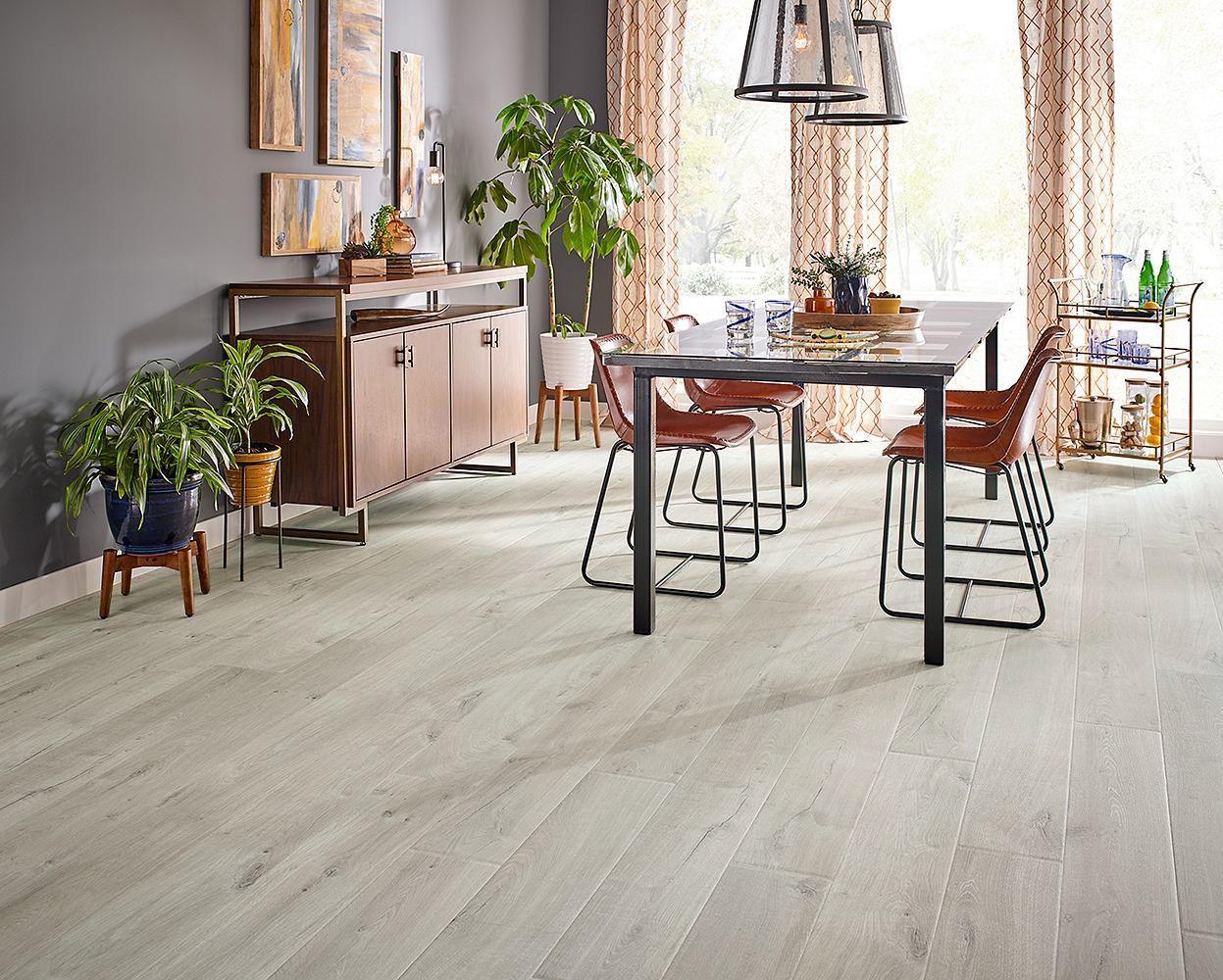 Comedor moderno con mesa de madera, sillas, plantas y suelo gris claro.