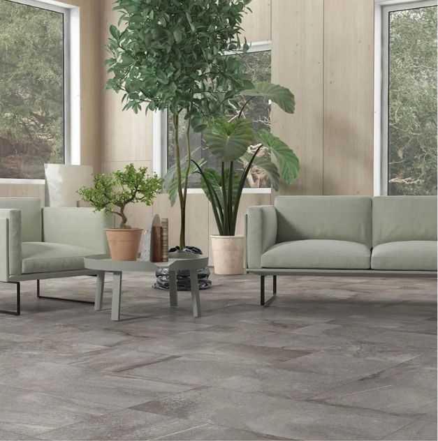 Sala de estar moderna con sofás de tonos claros, plantas en macetas y grandes ventanales sobre suelo de baldosas grises.