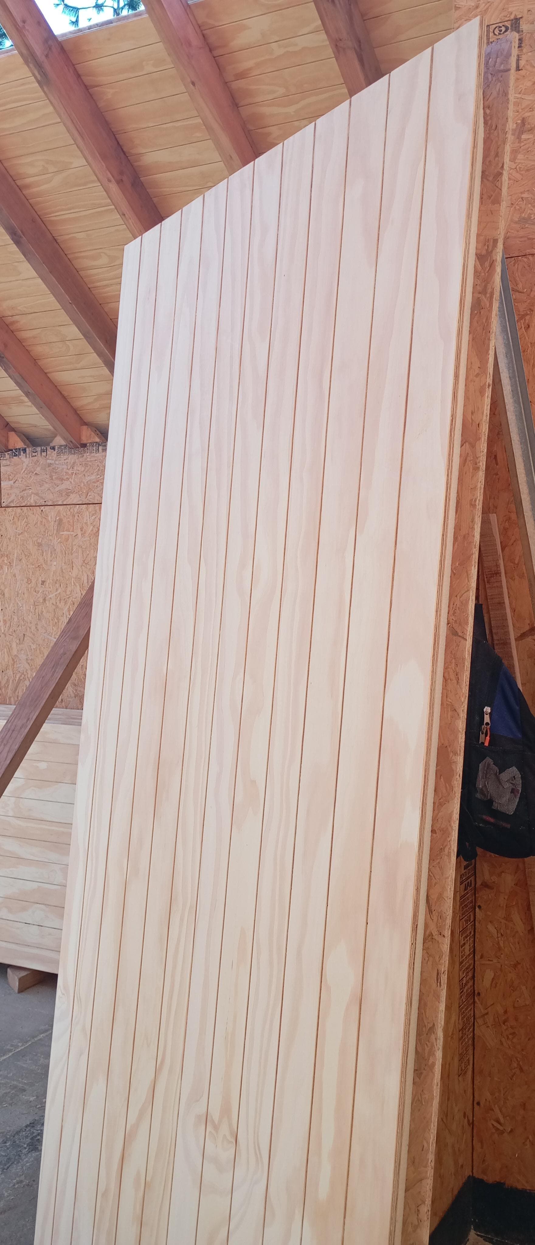 Panel de madera clara perforado apoyado en un taller con la estructura expuesta detrás.