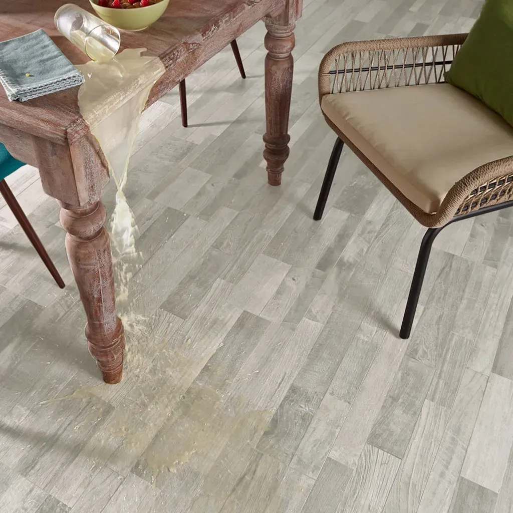 Mesa y silla rústicas de madera sobre un suelo gris claro, con una cinta colgando de la mesa y un cojín verde en la silla.
