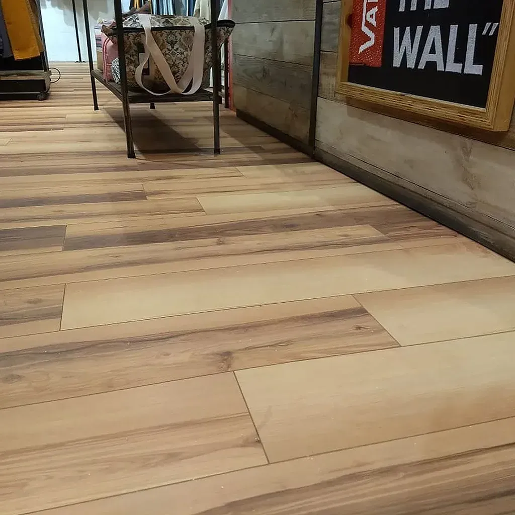 Suelo de tablones de madera en un interior industrial con un carrito y un letrero de pared visibles al fondo.