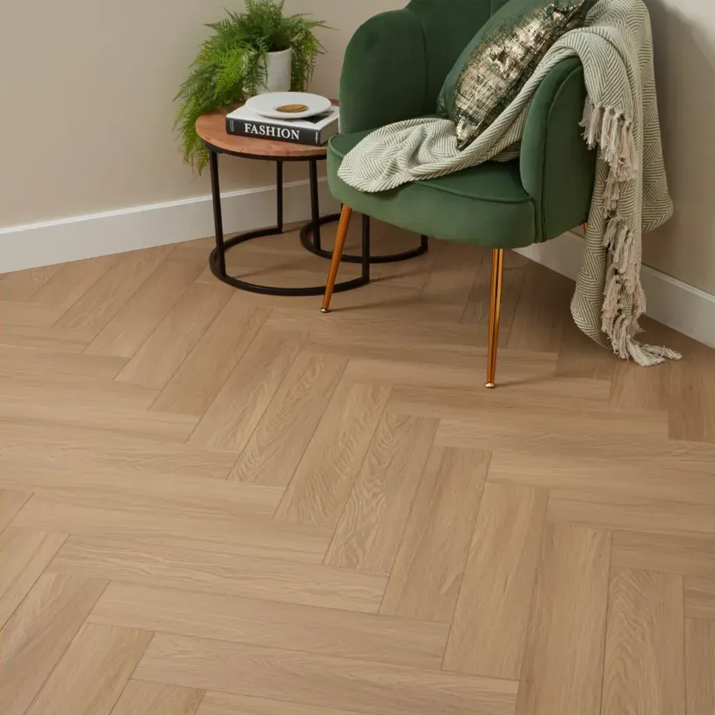 Suelo de madera gris claro con una mesita que sostiene un jarrón y una cesta, junto a una silla y una pila de libros.