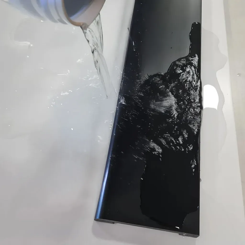 Agua vertiéndose de una taza sobre una superficie rectangular negra brillante sobre un fondo blanco.
