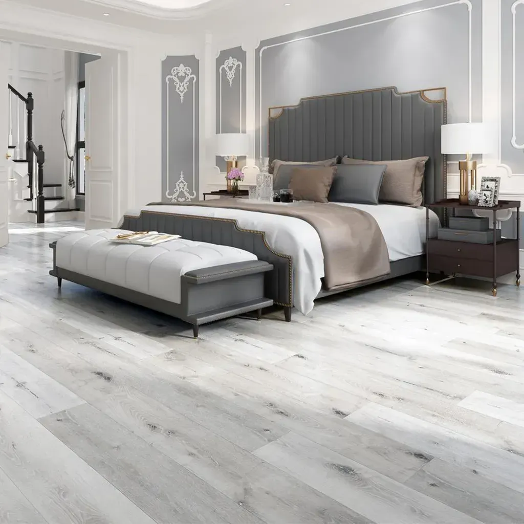 Elegante dormitorio gris con cama tapizada, banco, mesitas de noche y suelo de madera blanca.