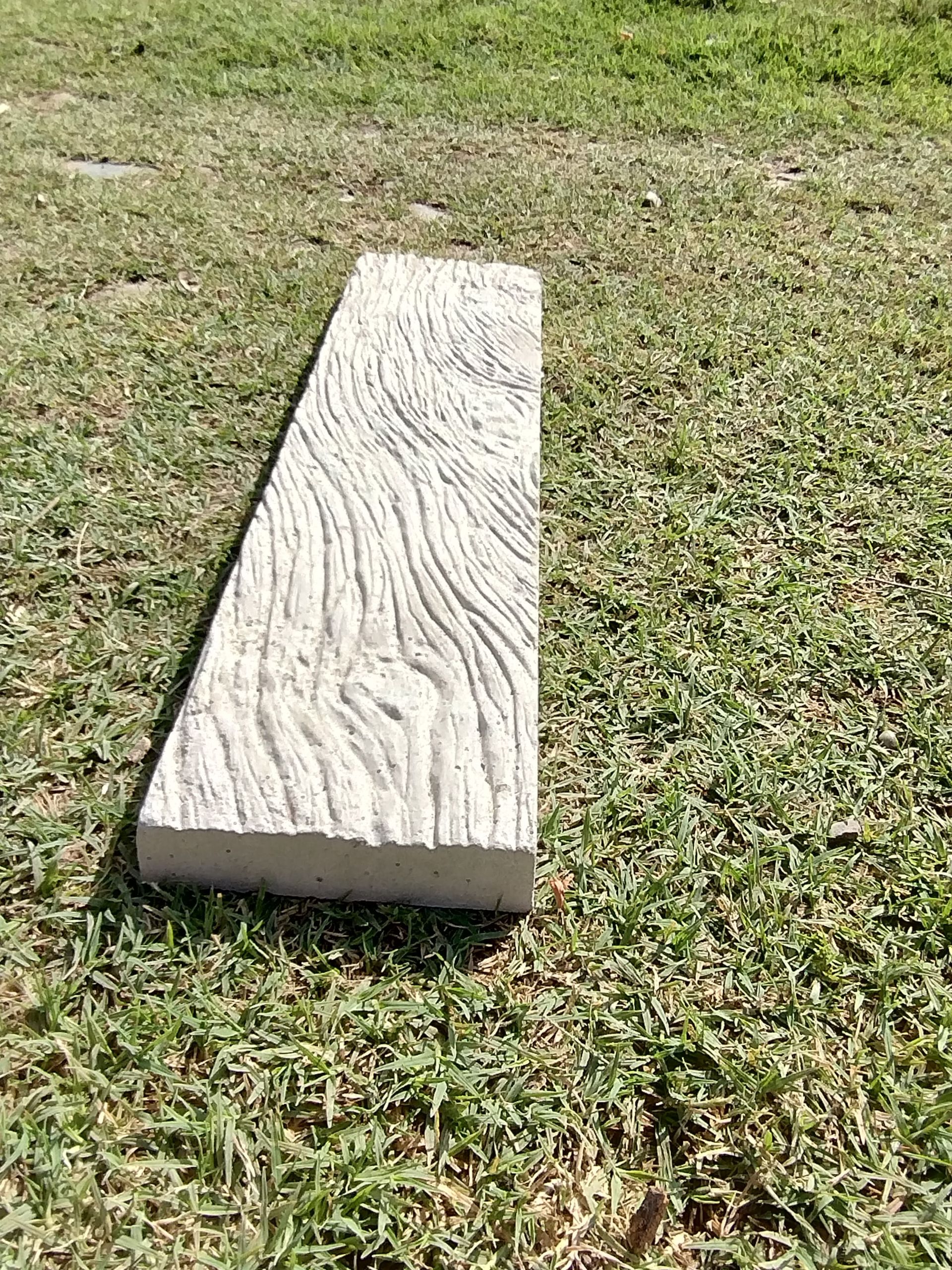 Una estrecha tabla de madera desgastada yace sobre un césped.