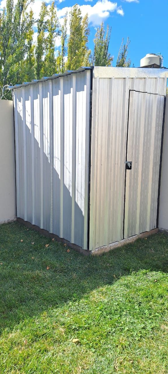 Un cobertizo de metal corrugado blanco en un patio trasero cubierto de césped, junto a un muro de hormigón