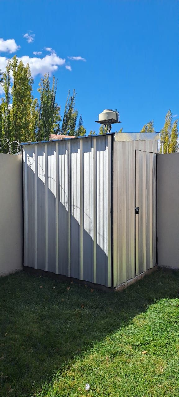 Un cobertizo de metal corrugado blanco en un patio trasero cubierto de césped, junto a un muro de hormigón
