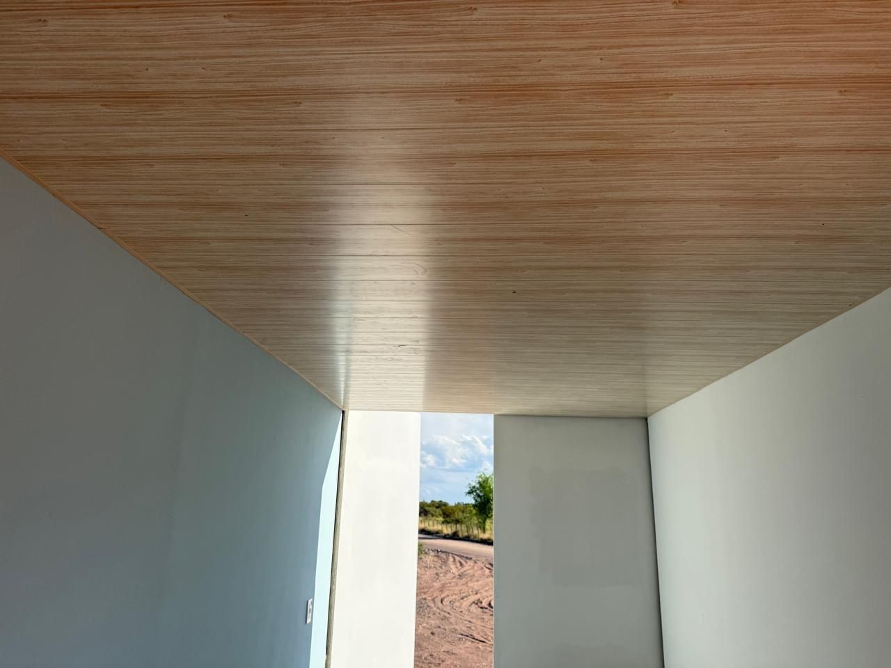 Habitación vacía con paredes azul claro, techo revestido de madera y luz solar en el suelo.