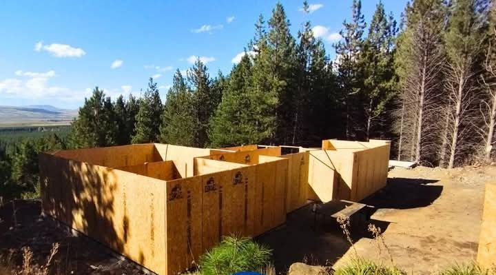 Obra en construcción con estructuras de madera contrachapada en las paredes, situada en una ladera