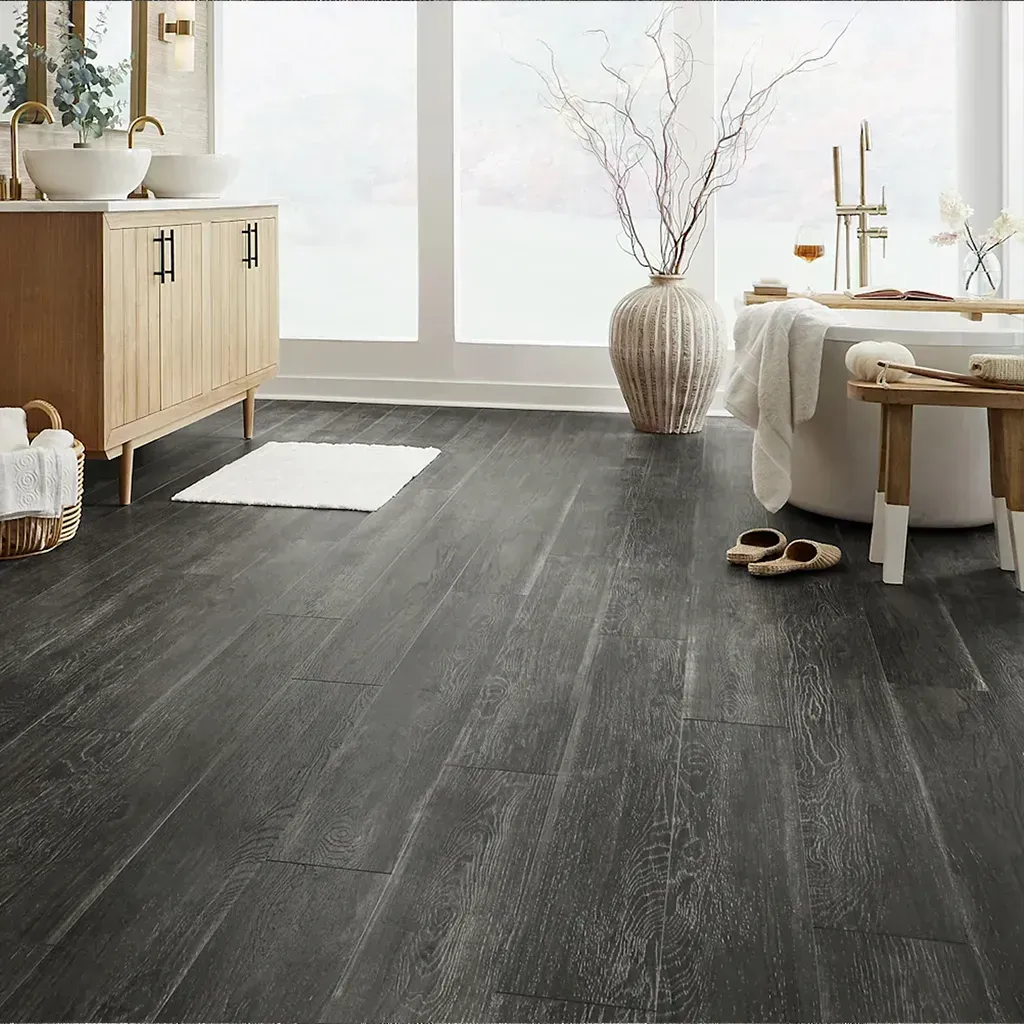 Habitación luminosa y minimalista con suelo de madera oscura, armario claro, banco y jarrón cerca de una ventana soleada.