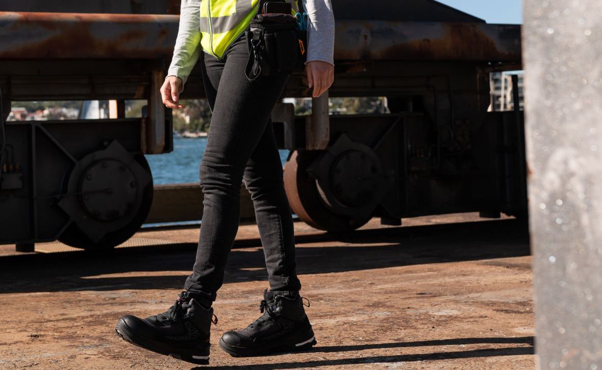 A person wearing black pants and black boots is walking on a dirt road.
