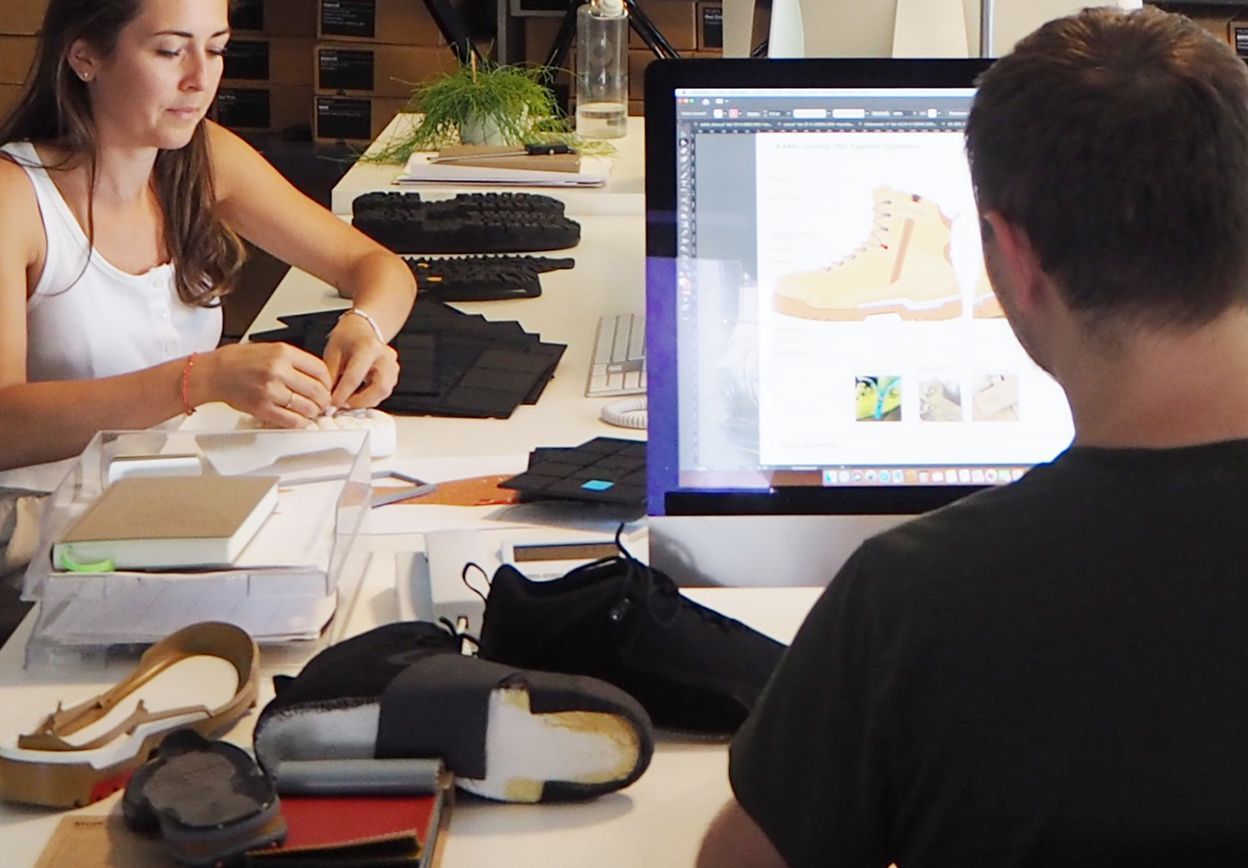 A man and a woman are sitting at a desk looking at a computer screen.