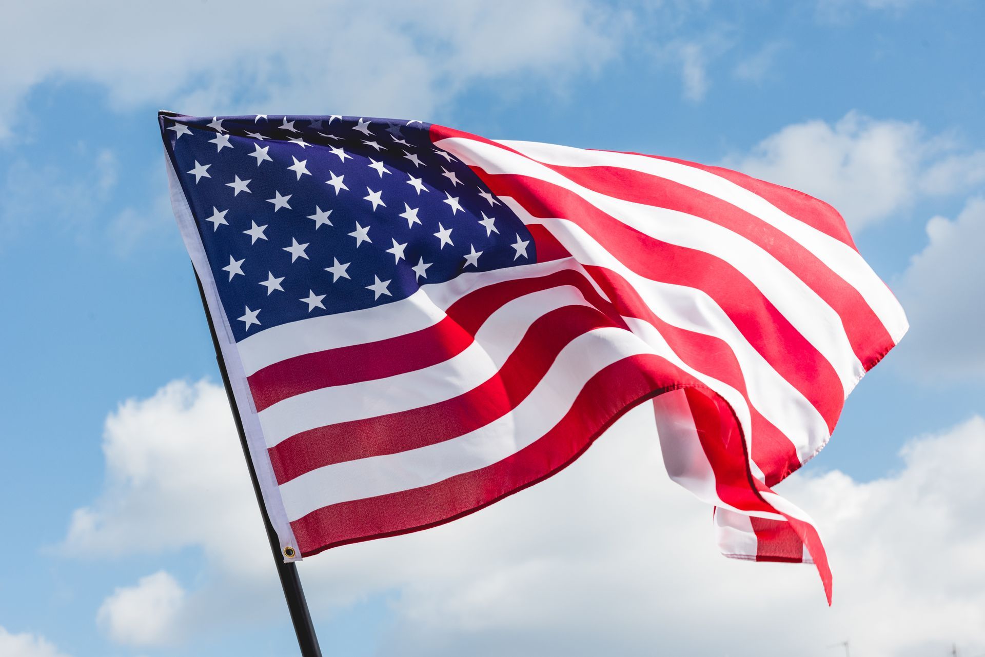 American flag waving against a blue sky with clouds American flag waving against a blue sky with clouds
