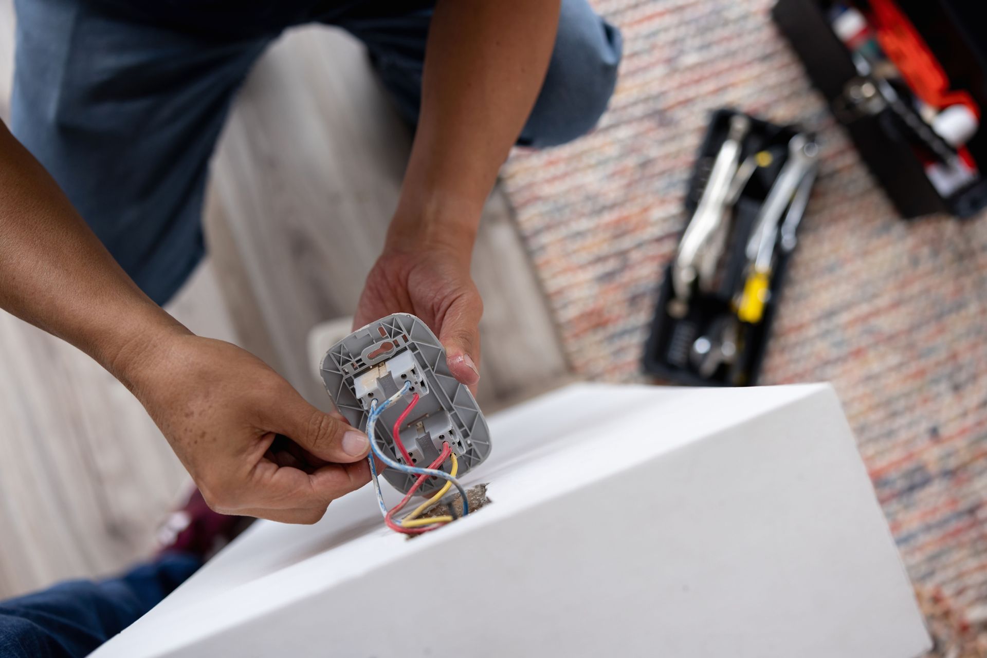 Person installing electrical outlet, hands holding wires, tools in case.