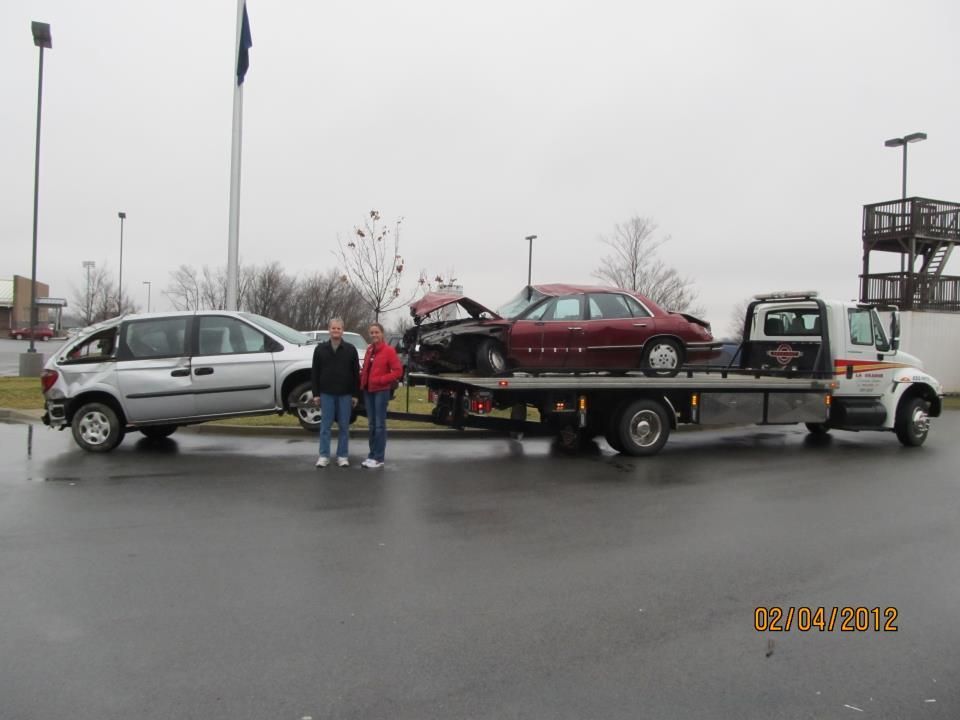 Two men standing in front of a tow truck with two cars on it