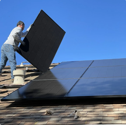 Worker installing black solar panels on a rooftop under a clear blue sky