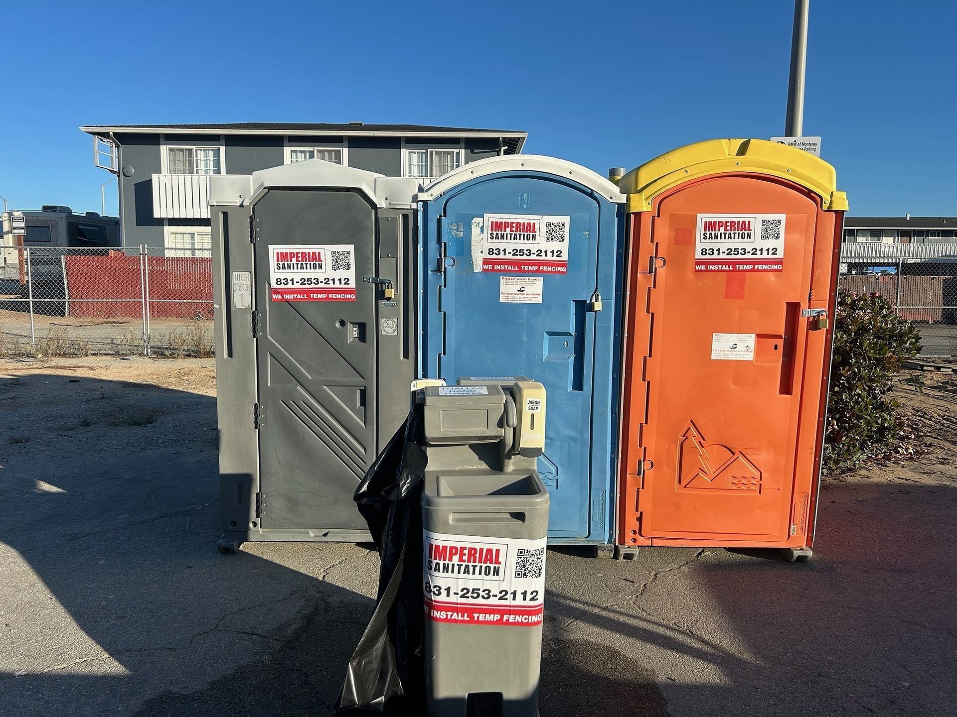 Three portable toilets are lined up next to each other in a parking lot.