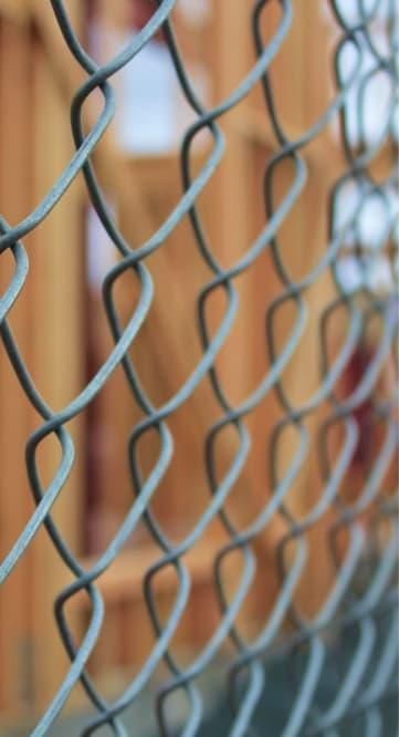 A close up of a chain link fence with a wooden fence in the background.