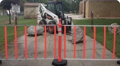 A bobcat is moving rocks in a driveway behind a barrier.