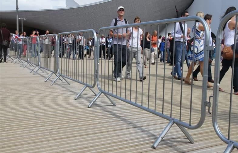 A group of people are walking behind a metal fence.