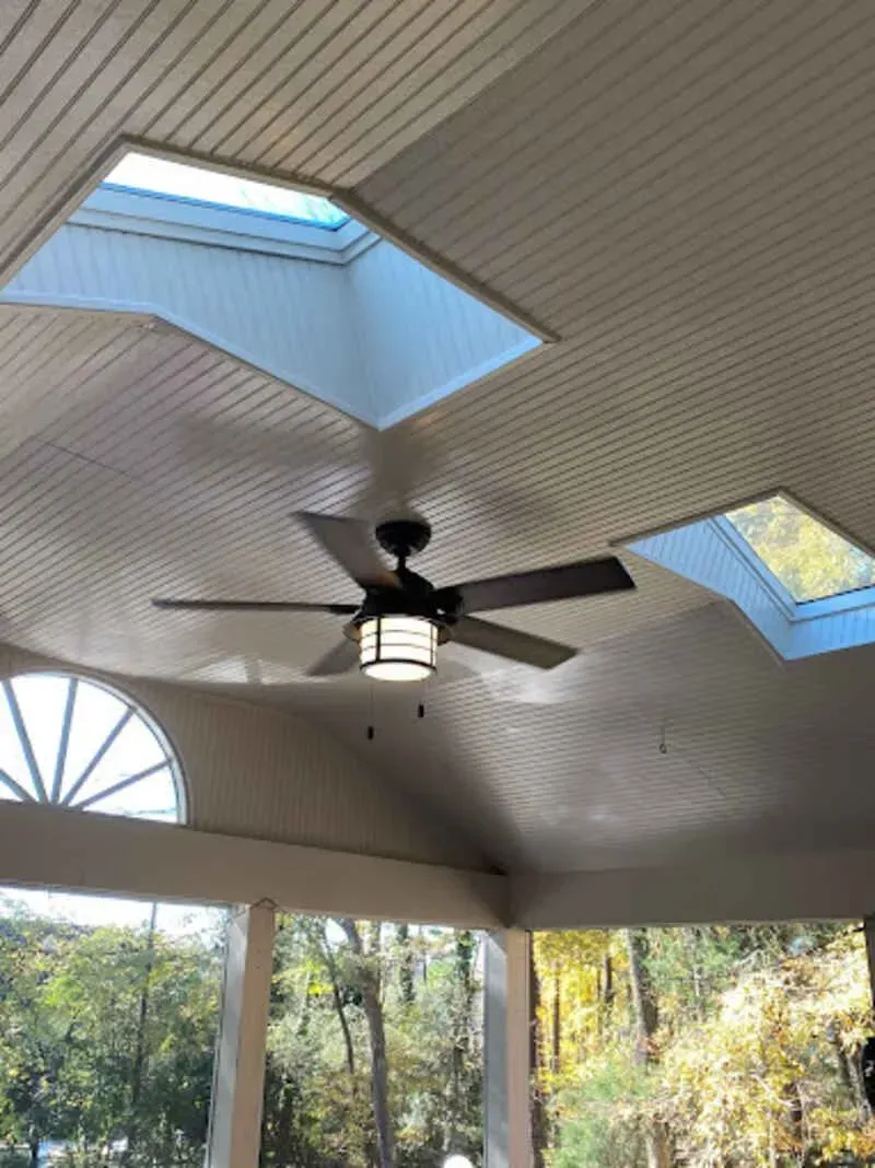 Ceiling with skylights and ceiling fan in an outdoor space, overlooking trees.