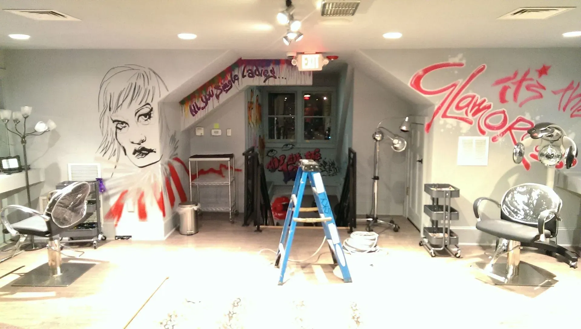 Salon interior with hair styling stations, ladder, artwork, and lights.