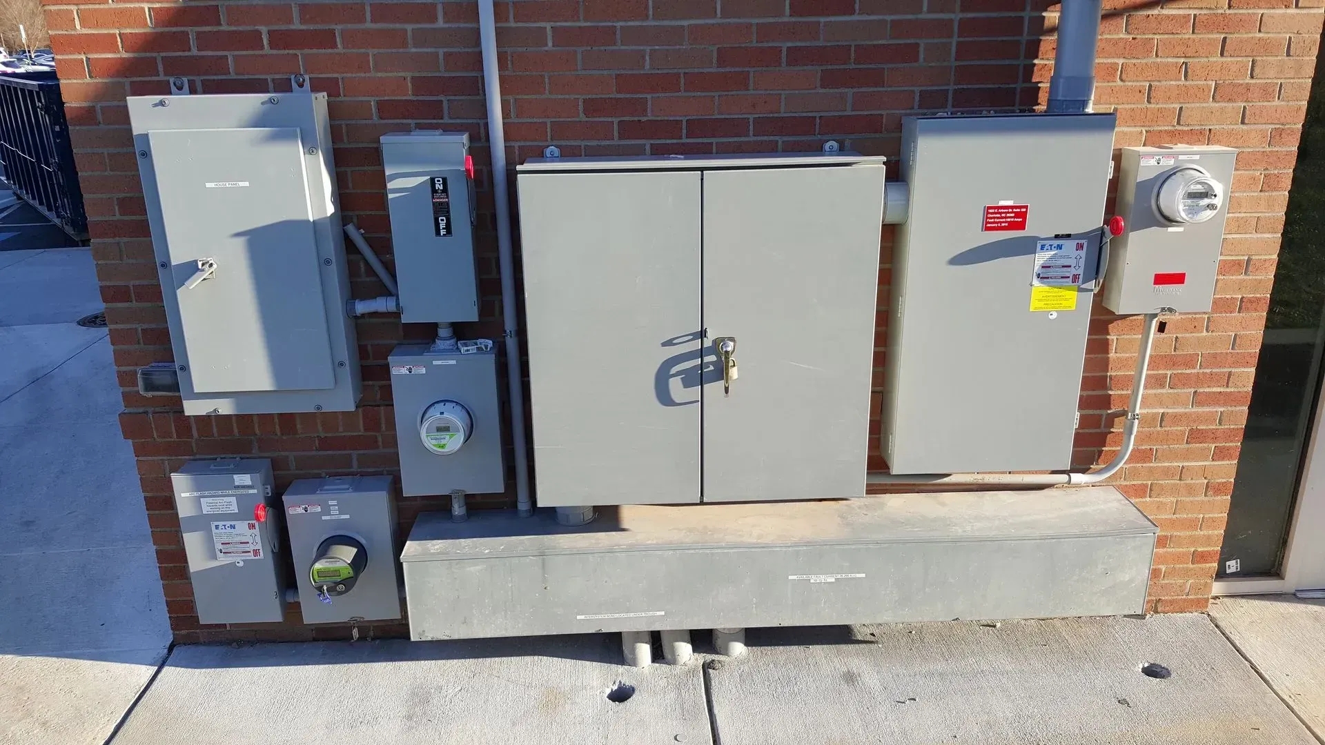 Electrical boxes mounted on a brick wall, including a large gray cabinet with a lock.