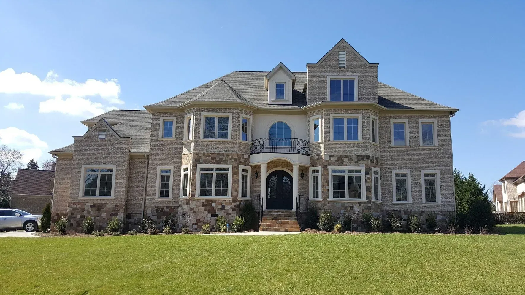 Large, multi-story stone house with many windows and a bright blue sky above.