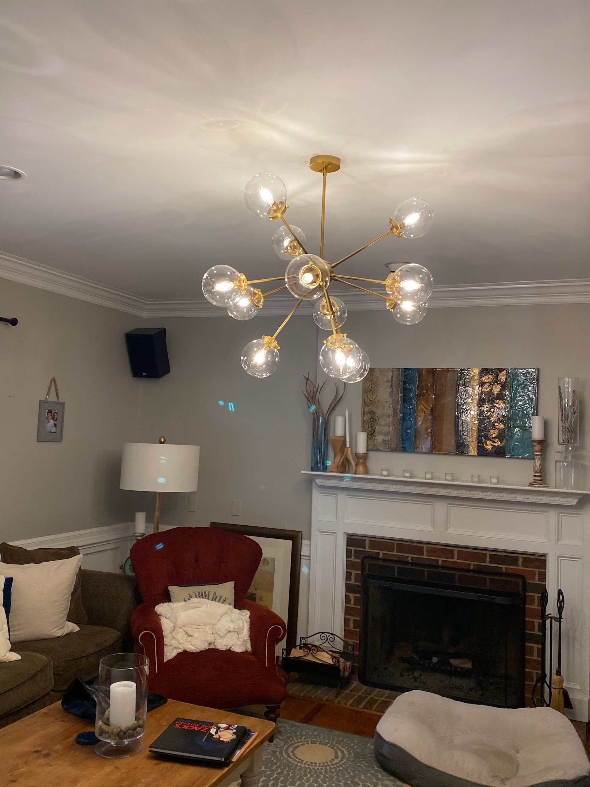 Living room with a gold chandelier, red chair, fireplace, and artwork.