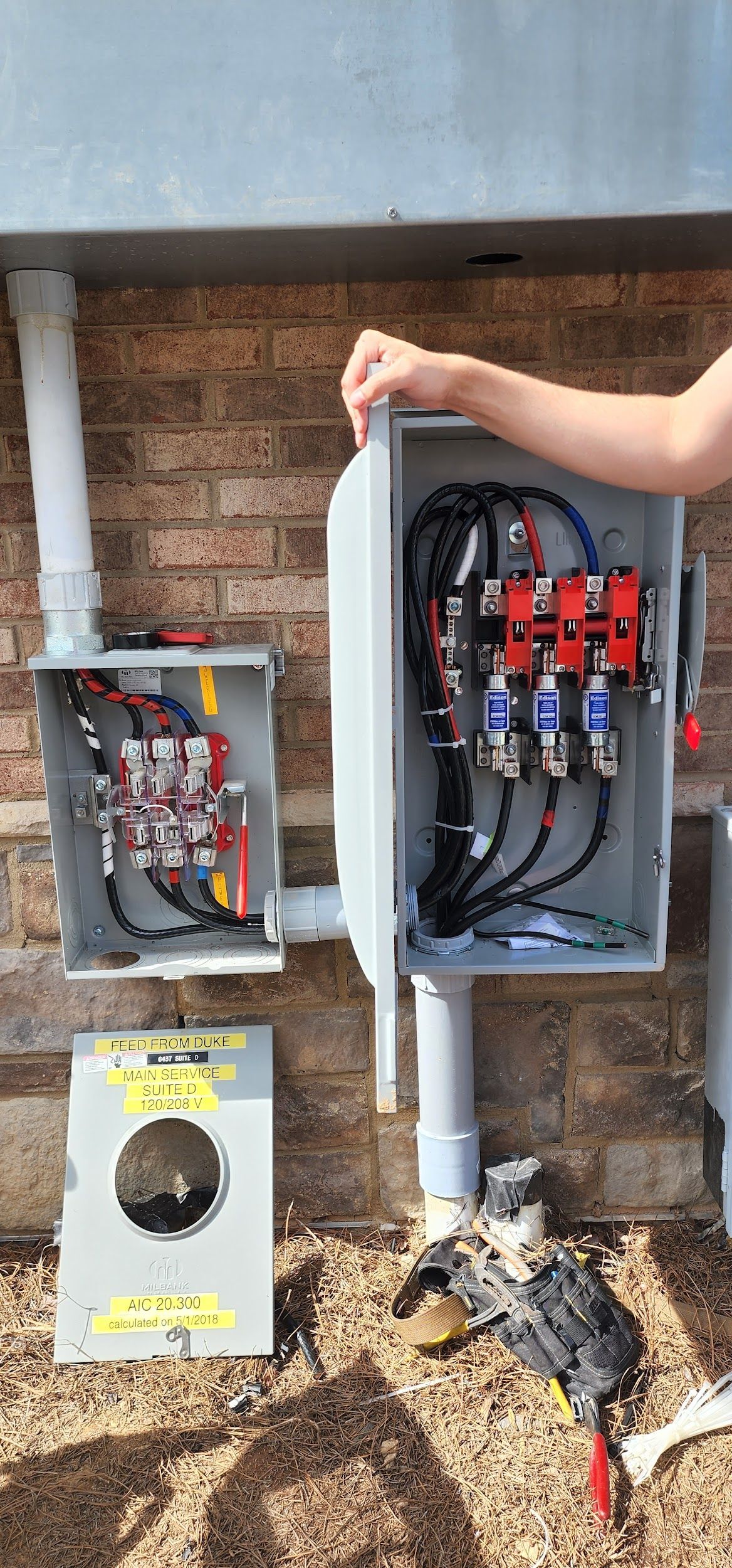 An open electrical box with wires and connectors on a brick wall, hand holding the box.