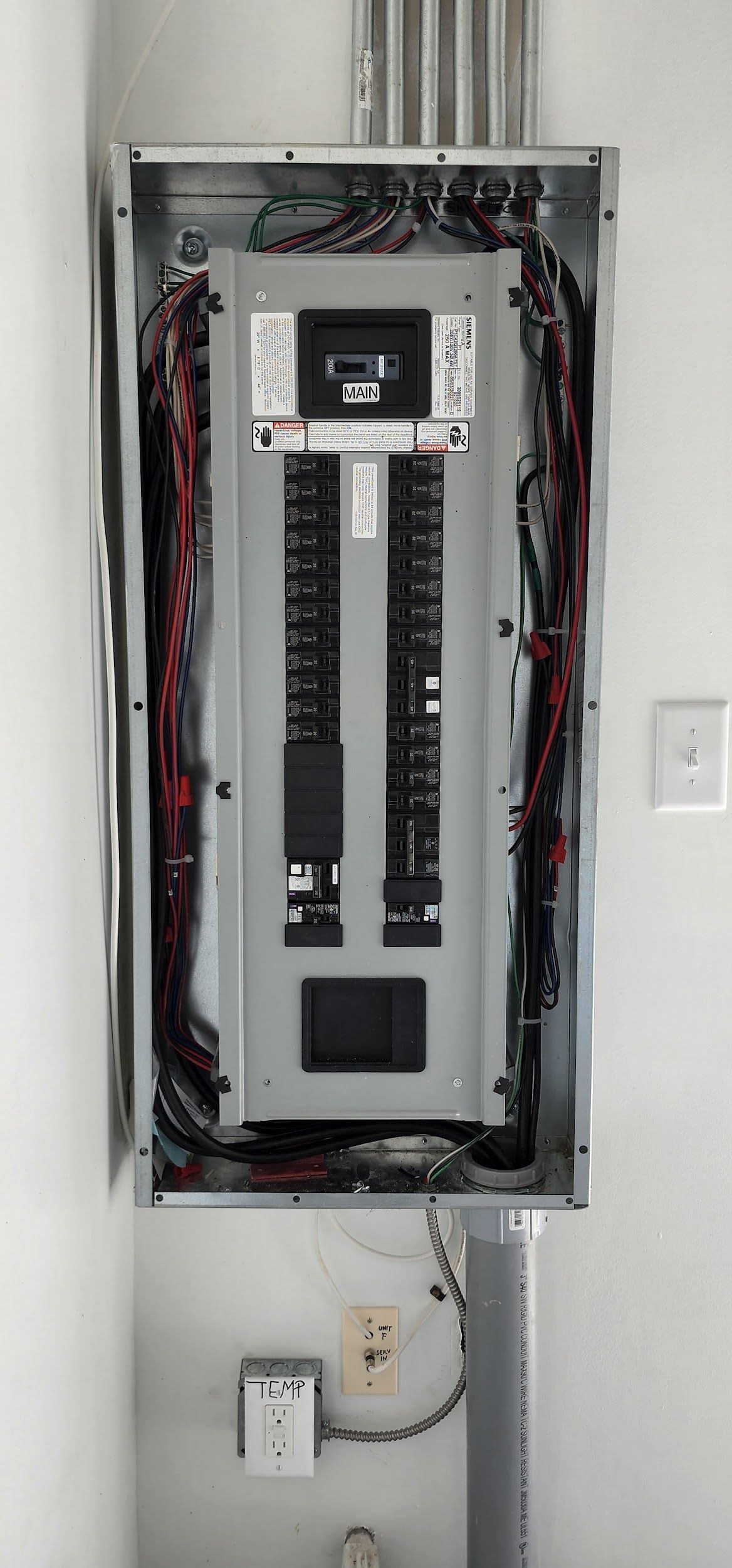 Electrical panel with wiring, mounted on a white wall.