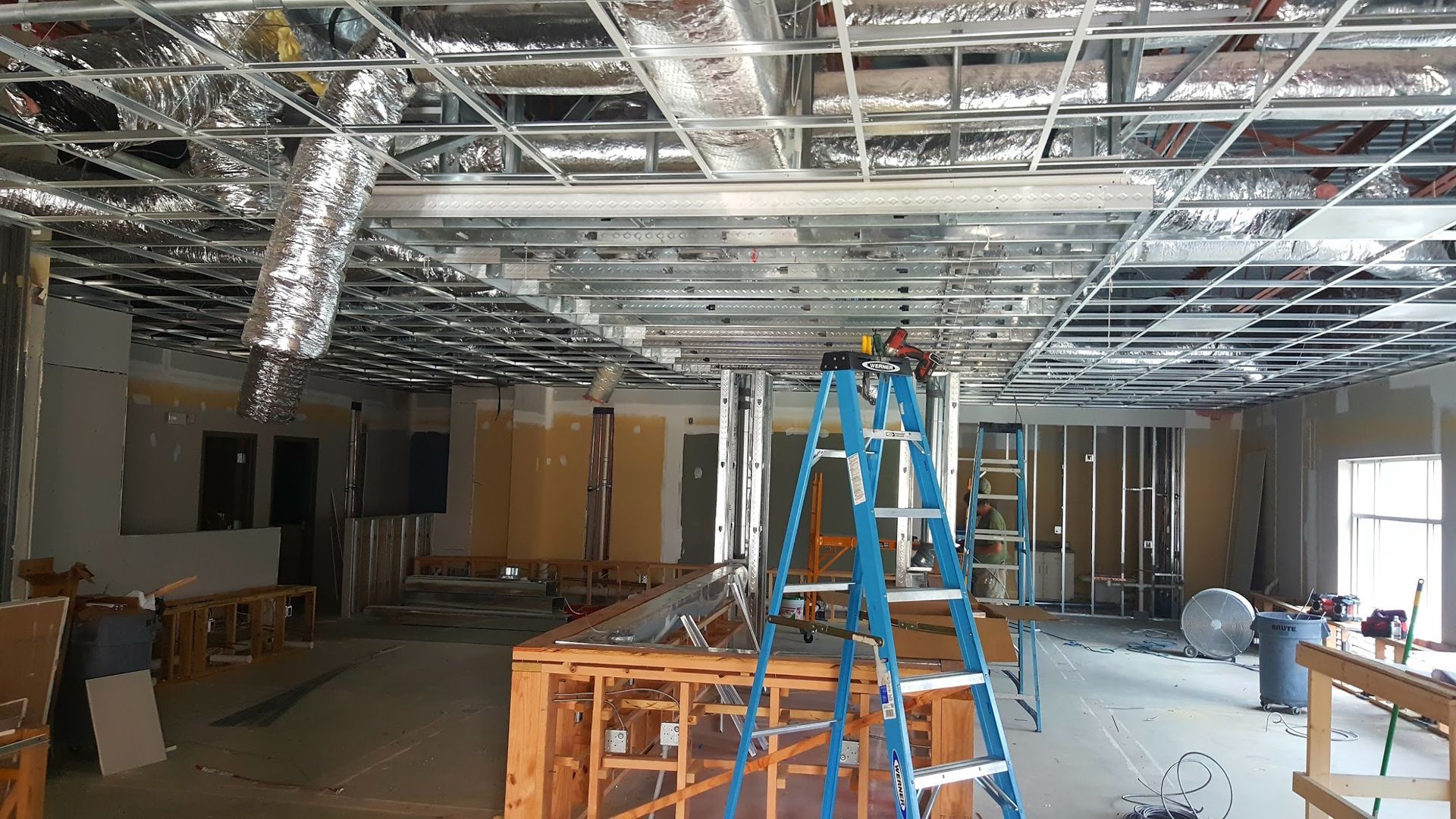 Interior construction site with metal framework, ductwork, and ladder.