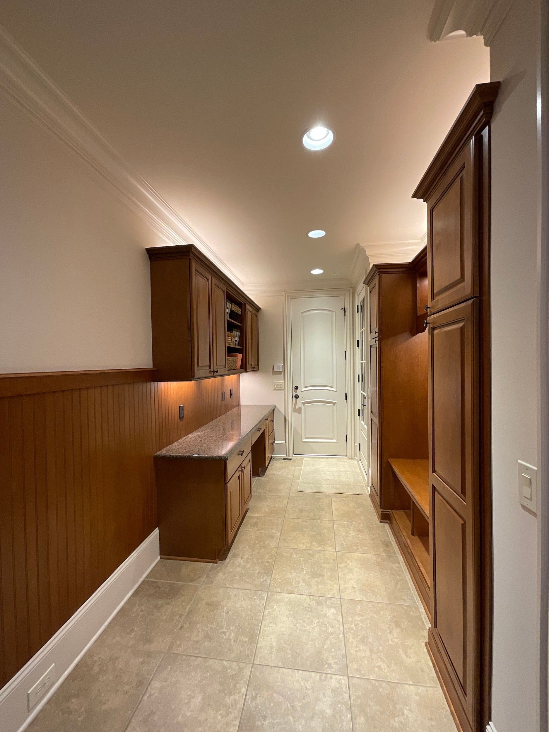Narrow hallway with wooden cabinetry, countertops, and a doorway at the end.