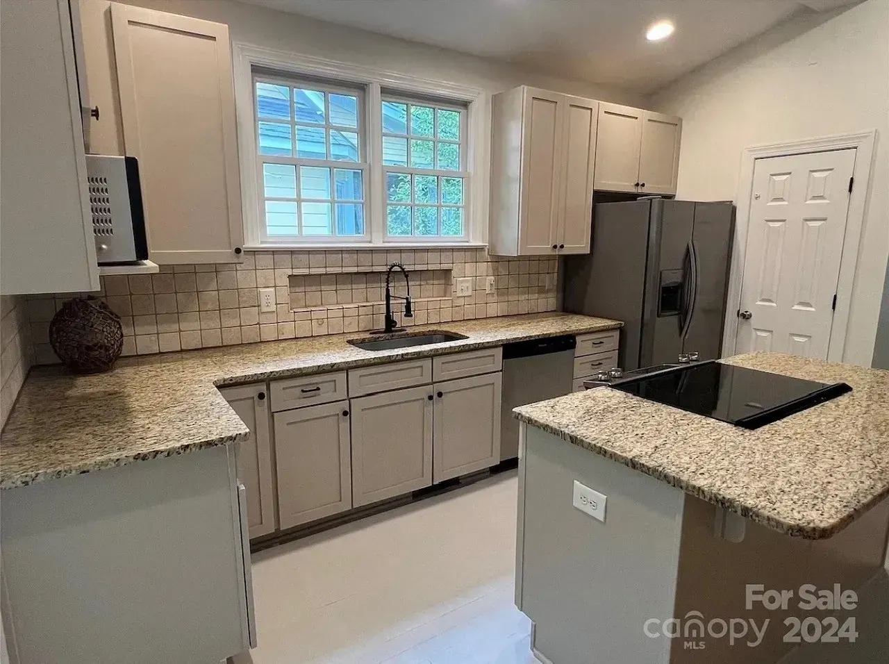 Modern kitchen with white cabinets, granite countertops, tile backsplash, and stainless steel appliances.