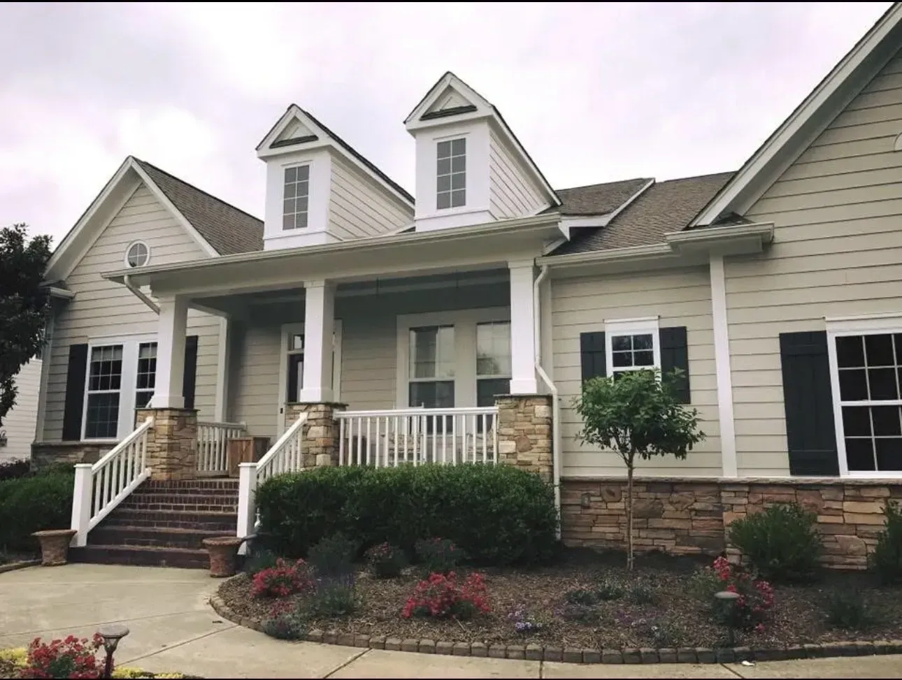 Suburban house with front porch, white siding, brick steps, and landscaped shrubs