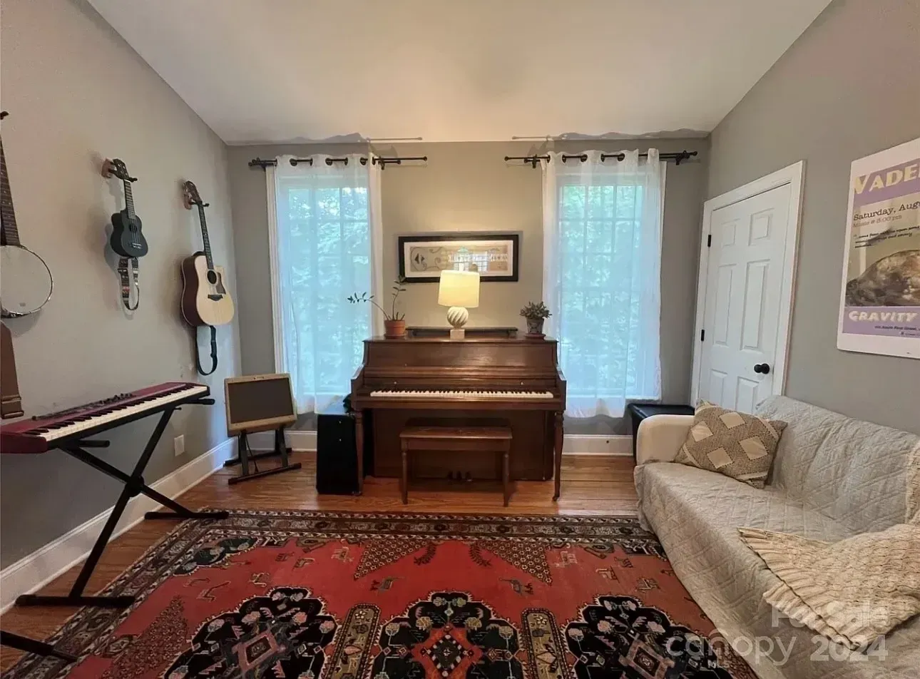 Living room with piano, sofa, keyboard, guitars, and tall windows with sheer curtains